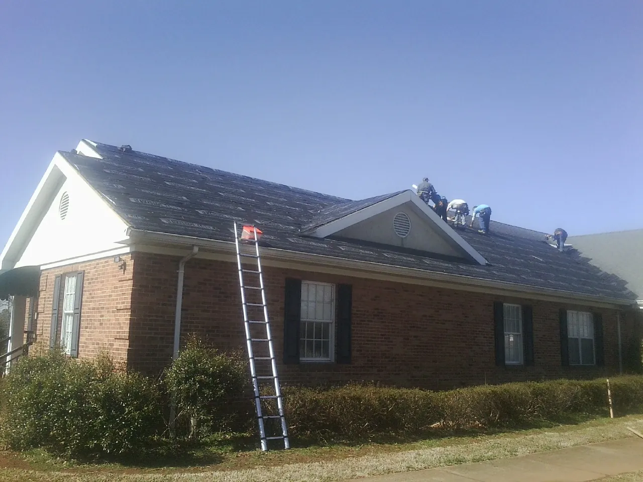 Crew tearing shingles off a brick ranch roof with a ladder set — Metal Roof Repair work by our crew in South River
