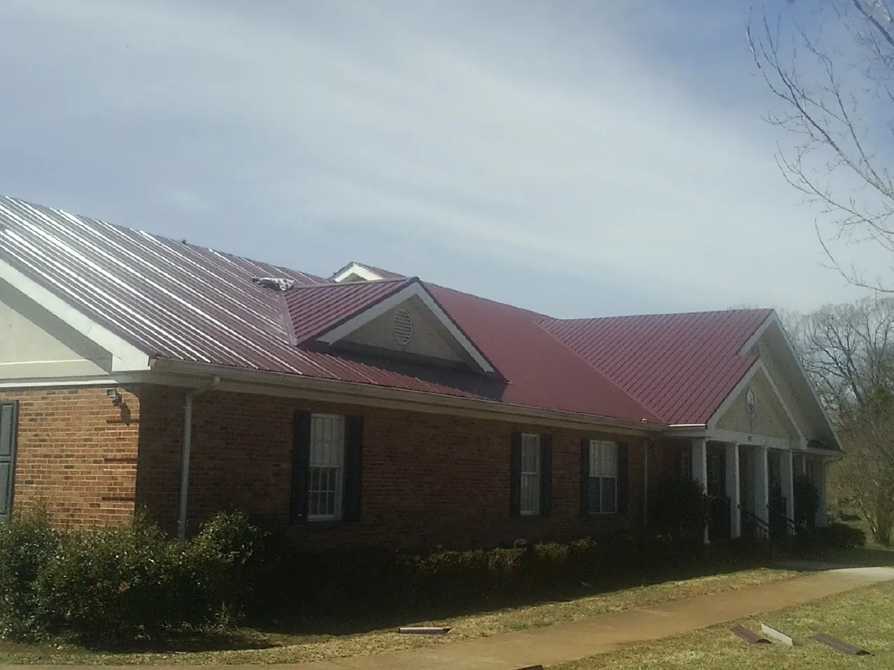 Red metal roof with gabled entries on a long brick building, from a Hail Damage Roof Repair job in South River