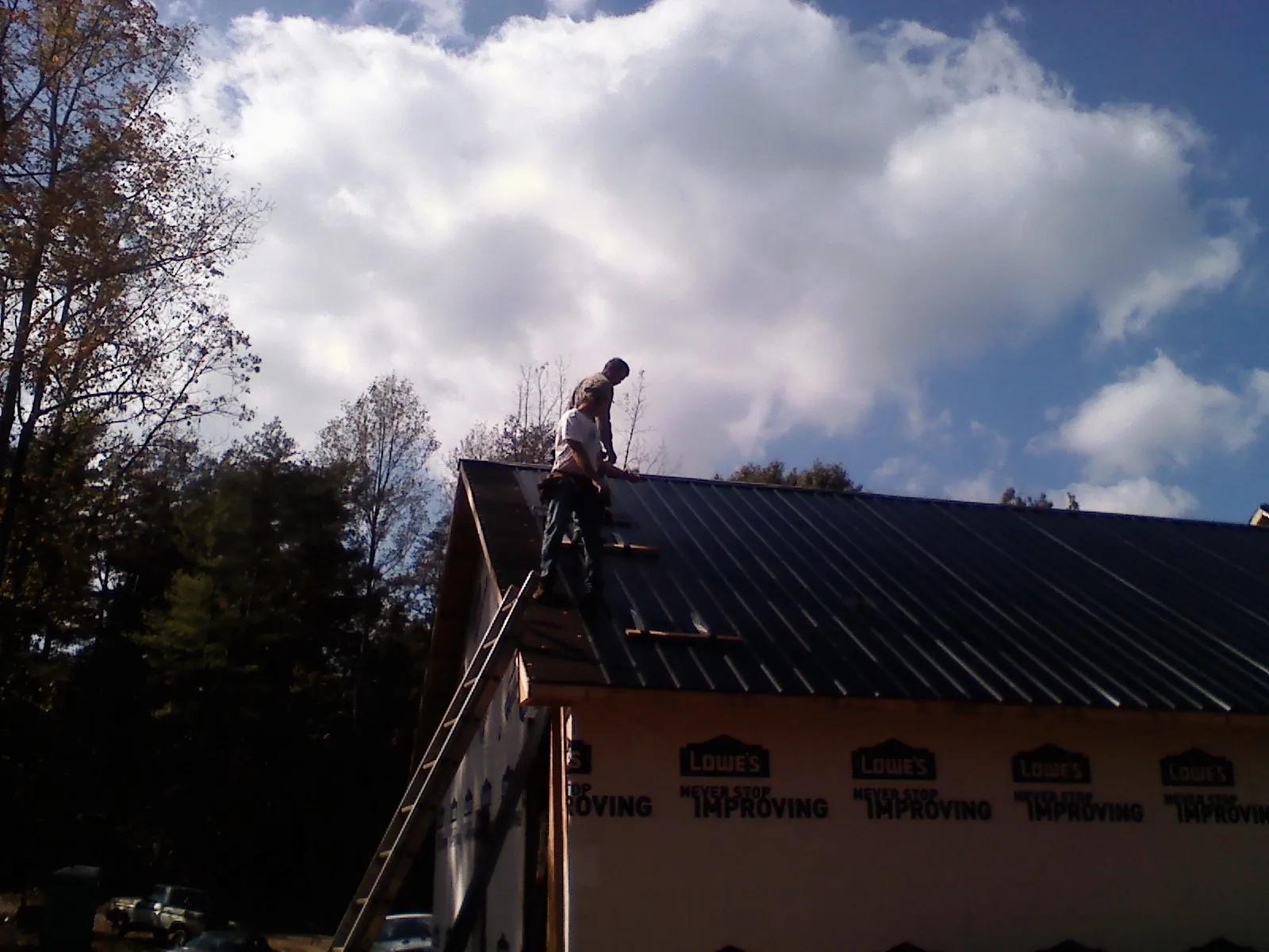 Roofer fastening dark metal panels high against a cloudy sky, from a Roof Inspection job in South River