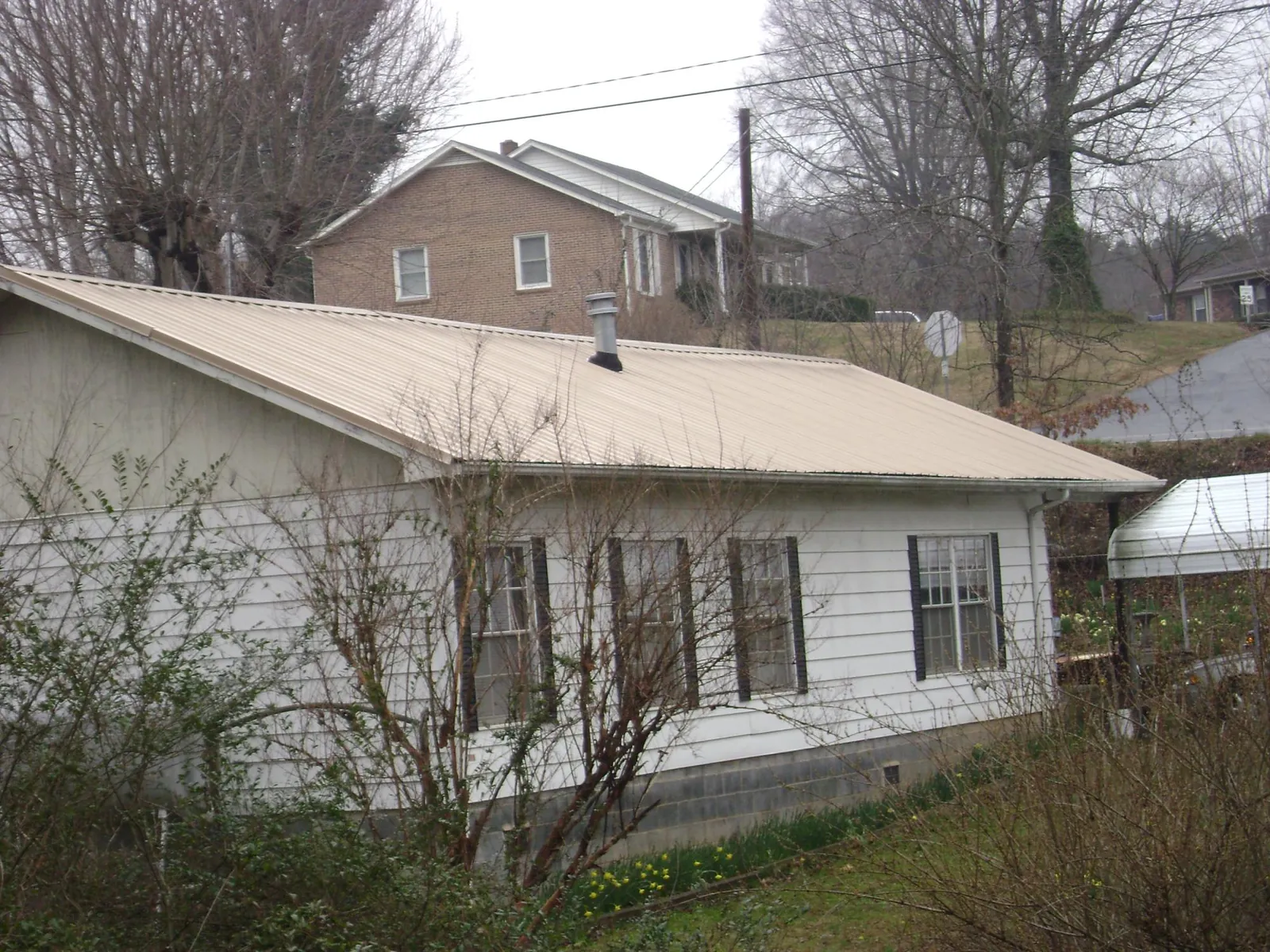 Tan metal roof on a white sided house set into a hillside — Commercial Roofing by Roofing Brothers in South River